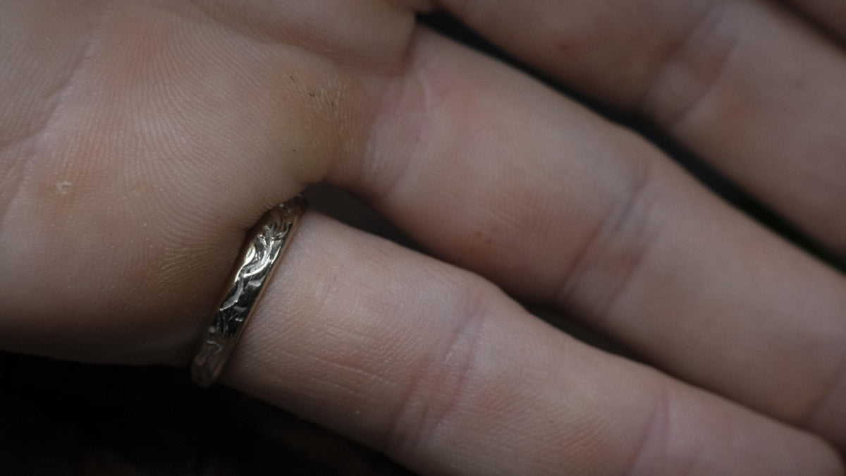 Side view of the patterned gold ring band worn on a finger